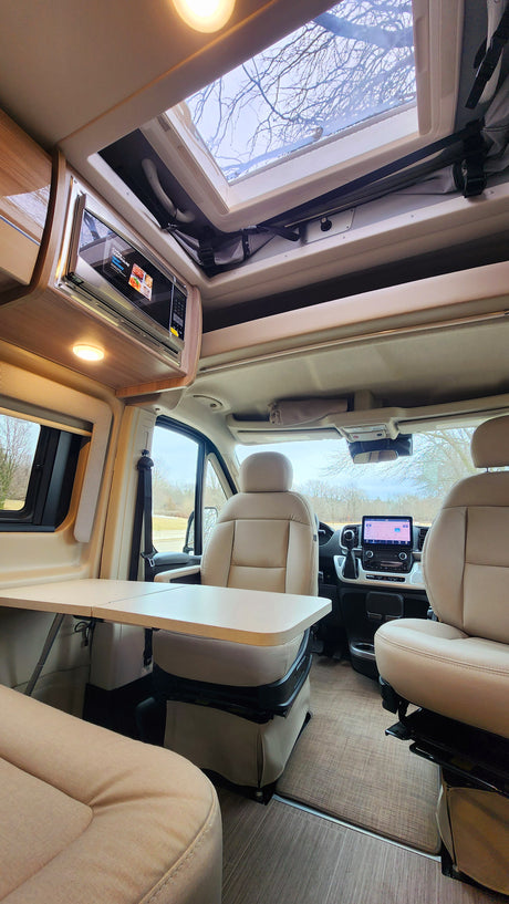 Spacious RV rental interior with swiveling seats, fold-out table, overhead microwave, and large skylight.