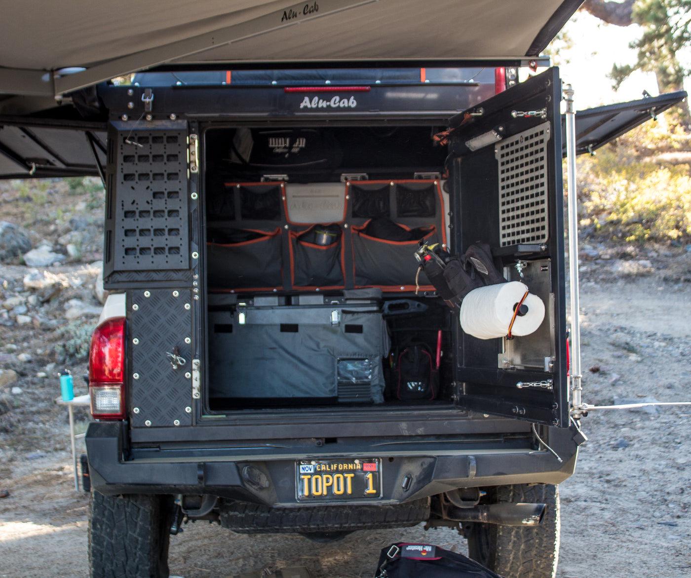 Alu-Cab truck camper setup, perfect for an rv rental adventure. Shows open rear with organized storage, fridge, and awning. — photo 9