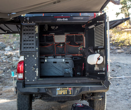 Alu-Cab truck camper setup, perfect for an rv rental adventure. Shows open rear with organized storage, fridge, and awning.
