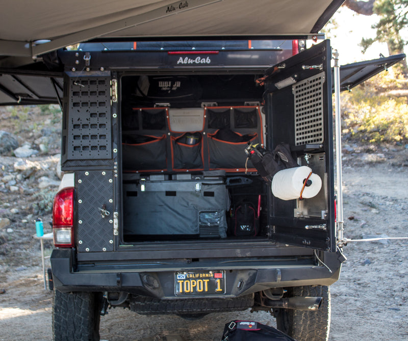 Alu-Cab truck camper setup, perfect for an rv rental adventure. Shows open rear with organized storage, fridge, and awning. — photo 9