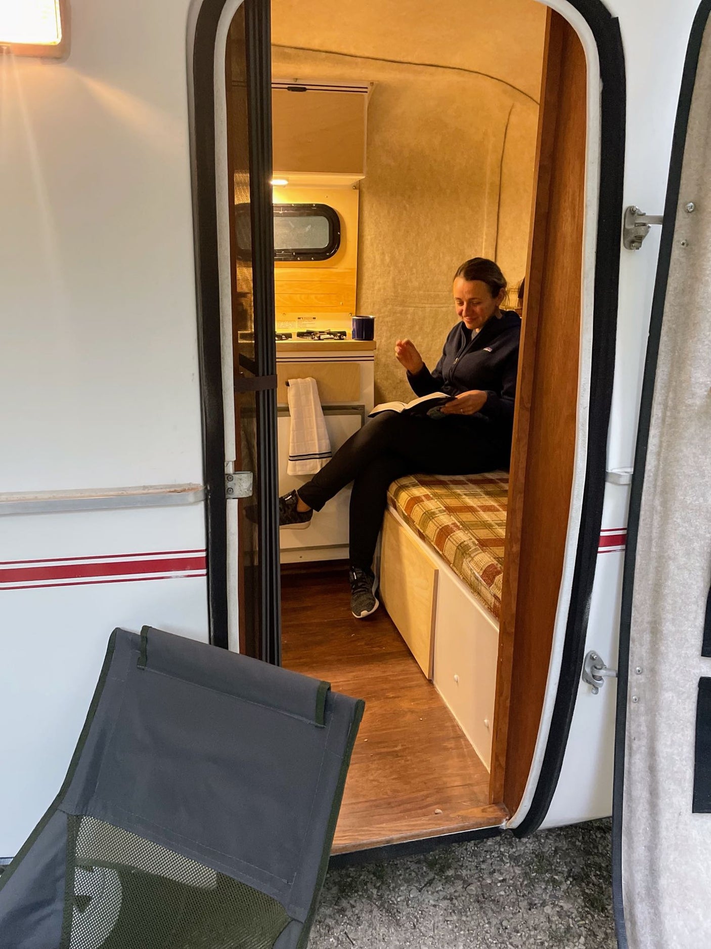 Relaxing inside a compact RV rental: woman reads on a cozy plaid bench, inviting adventure.