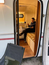 Relaxing inside a compact RV rental: woman reads on a cozy plaid bench, inviting adventure.