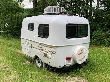 White Scamp travel trailer, a compact RV rental, parked on grass. Ready for your next camping adventure.