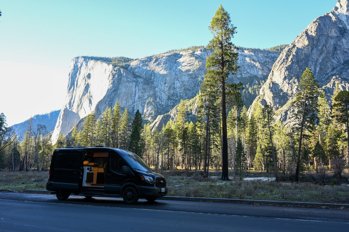 Black rv rental van parked in a scenic mountain valley, revealing a cozy interior. Tall pines frame the majestic cliffs. — photo 2