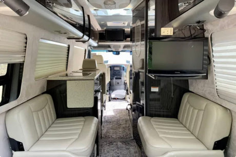 Spacious RV rental interior featuring comfortable seating, a compact kitchen, and TV for enjoyable travels.