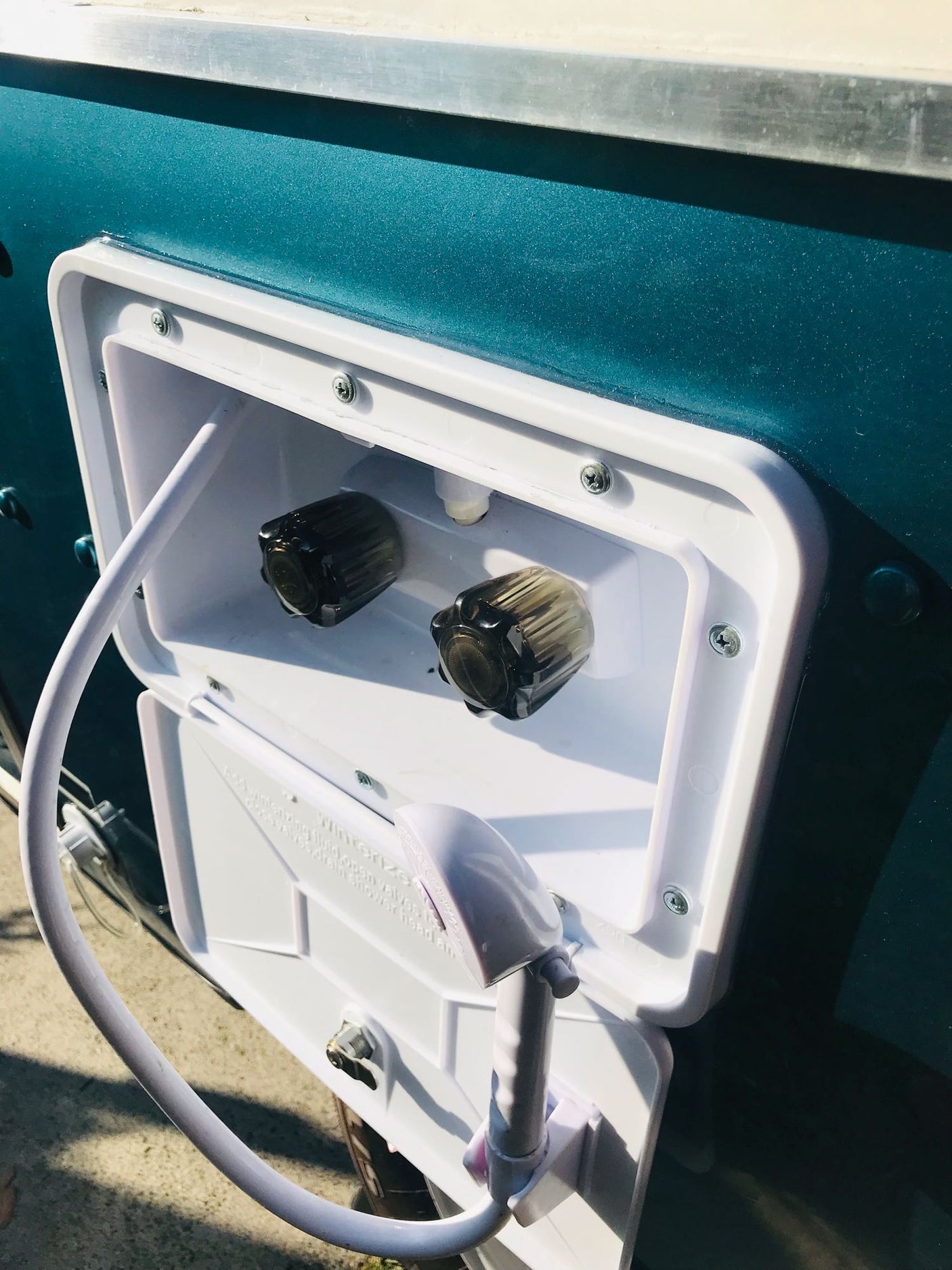 Open RV outdoor shower on a teal RV rental, showing knobs and hose for easy wash-offs.