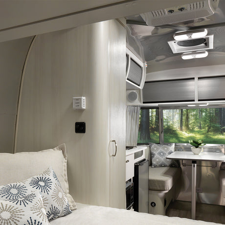 Bright rv rental interior featuring a bed, compact kitchen, and dining area with forest views.