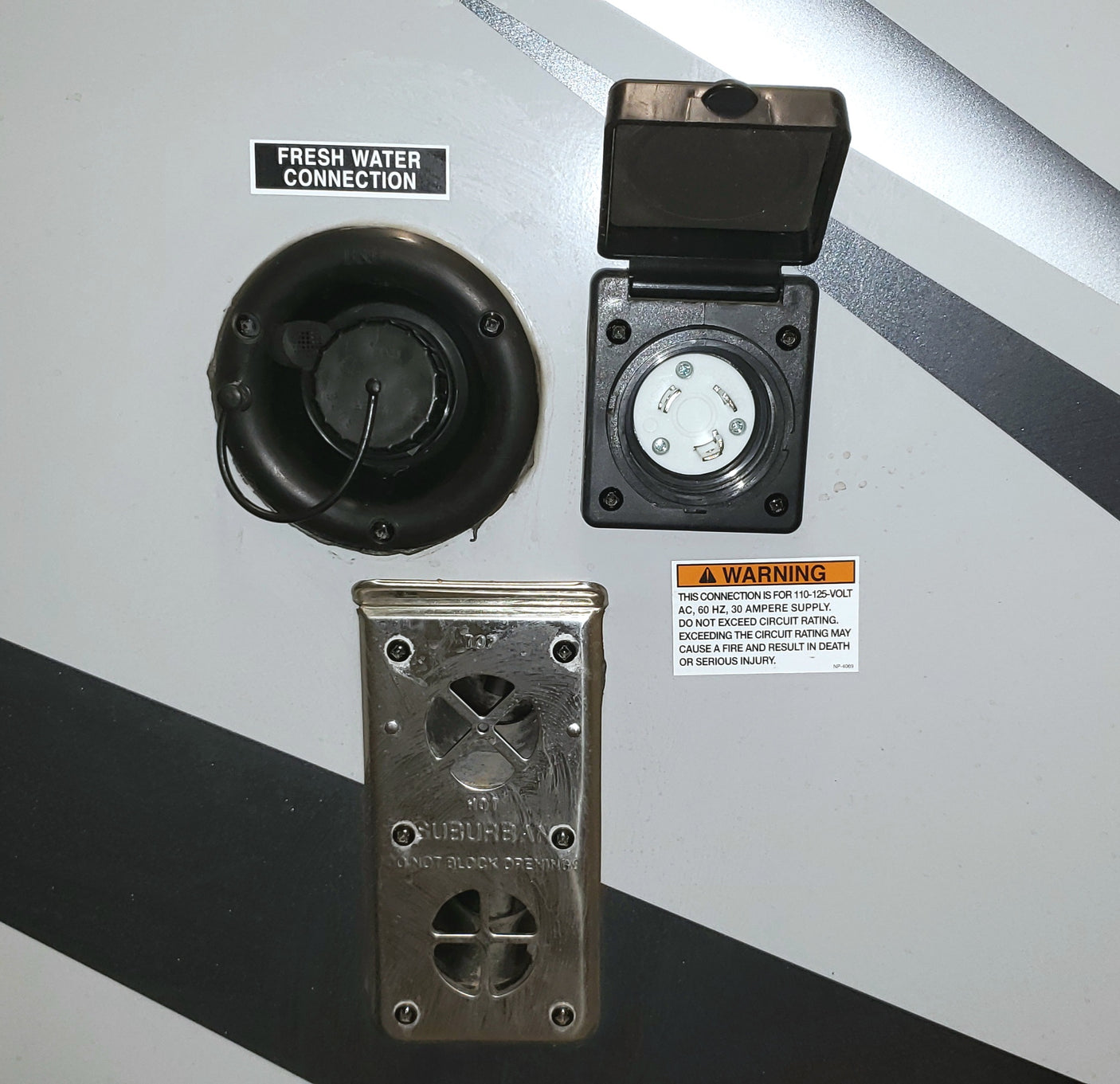 RV rental exterior connections: fresh water, 30-amp electrical power inlet, and a Suburban furnace vent.