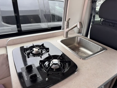 RV rental kitchen: compact two-burner stove, sink, & faucet for easy cooking on your road adventures.