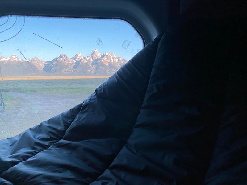  mossy forest view outside.|Relax in your RV rental! Cozy camper van interior shows a person on bed with coffee — photo 10
