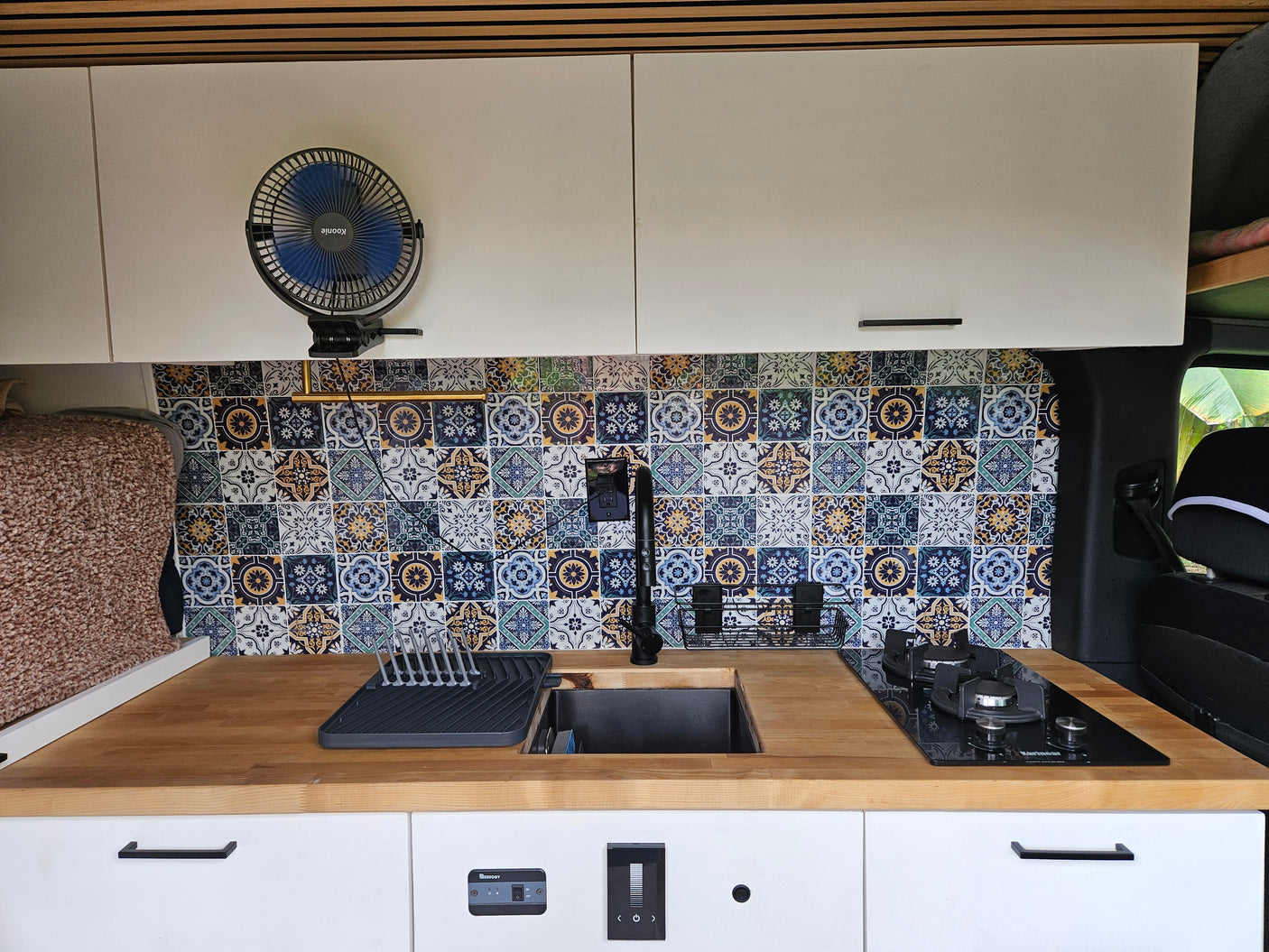 RV rental interior features a compact kitchen with a vibrant tiled backsplash, wooden counter, sink, stove, and white cabinetry.