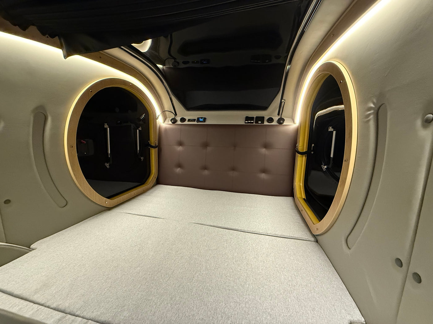 Cozy, modern sleeping area inside an rv rental, featuring a bed, padded headboard, and dual circular entryways with lighting. — photo 15