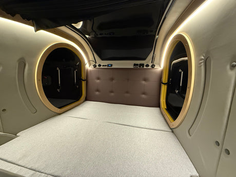 Cozy, modern sleeping area inside an rv rental, featuring a bed, padded headboard, and dual circular entryways with lighting.