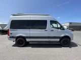 Side view of a silver Mercedes-Benz Sprinter "Tranquility" camper van, available for RV rental, parked on asphalt.