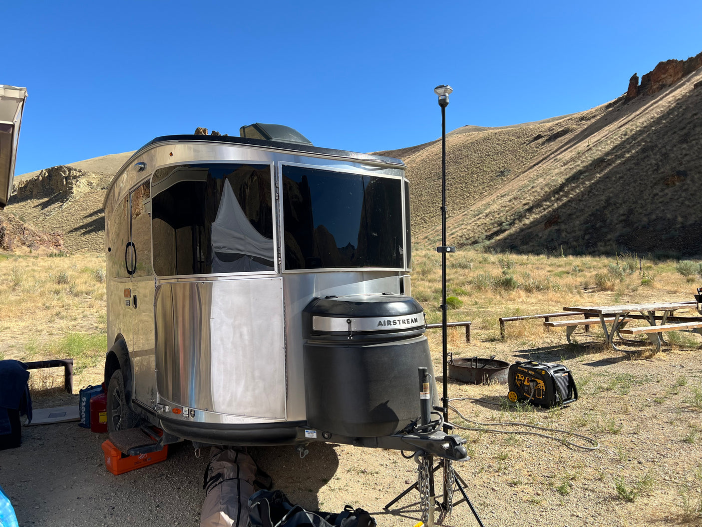 Silver Airstream RV rental shines in a scenic, dry campsite with hills, a generator, and a tall antenna.
