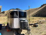 Silver Airstream RV rental shines in a scenic, dry campsite with hills, a generator, and a tall antenna.