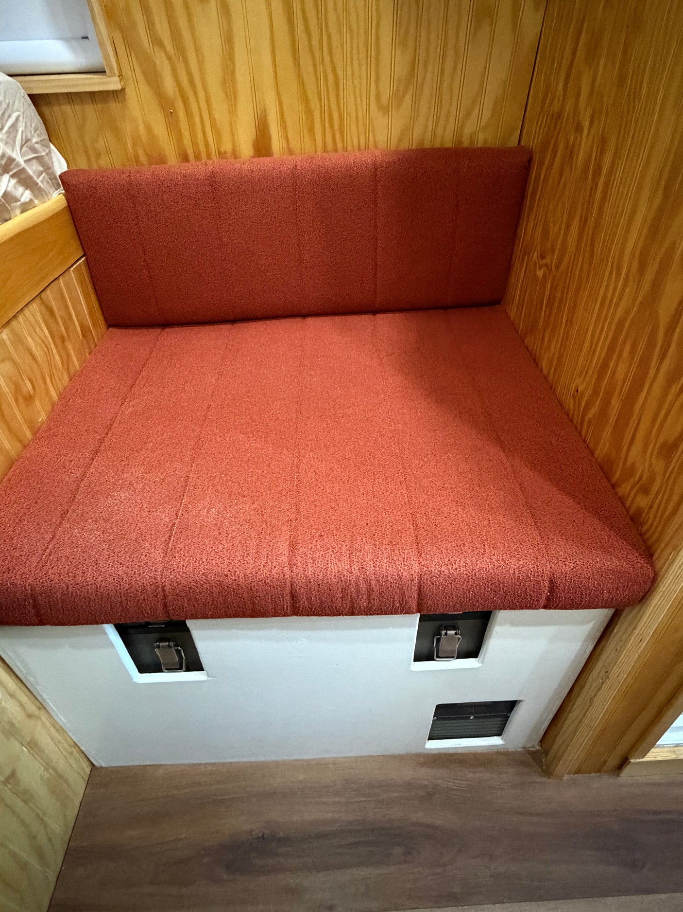 Cozy orange cushioned bench and backrest in an rv rental, featuring wood paneling & under-seat storage with latches.