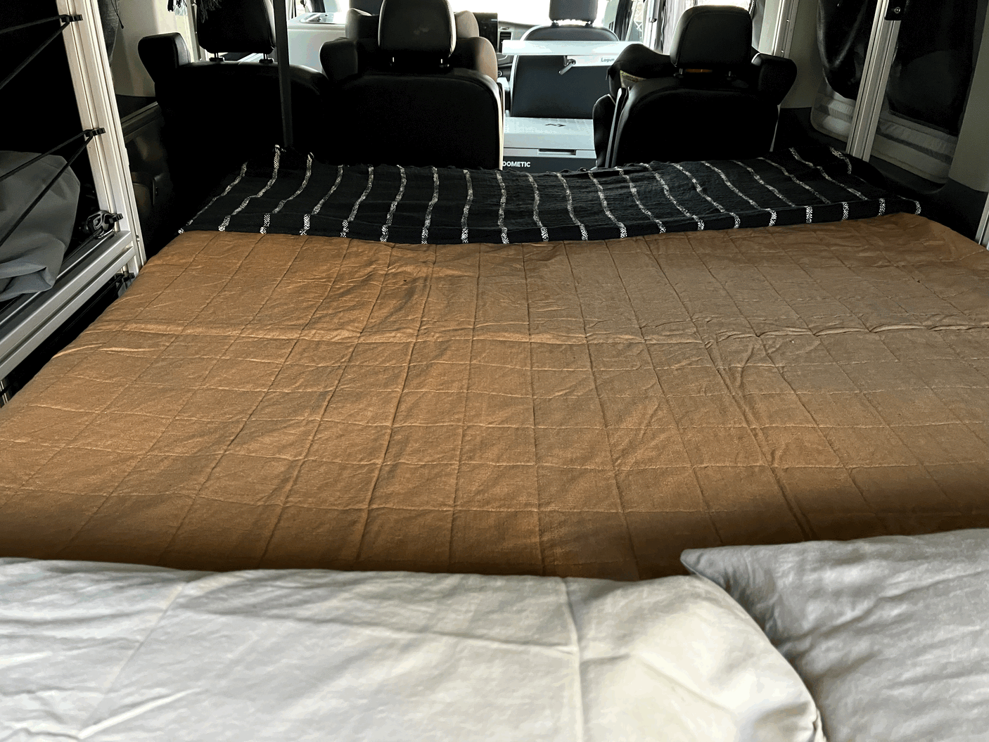Cozy RV rental interior showcasing a comfortable bed, black striped blanket, and a Dometic portable fridge.