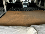 Cozy RV rental interior showcasing a comfortable bed, black striped blanket, and a Dometic portable fridge.