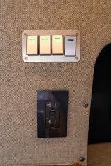 Essential controls in an RV rental: four switches (three with green lights) and a black GFCI outlet on a durable fabric wall.