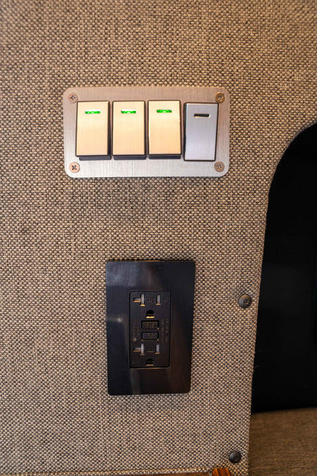 Essential controls in an RV rental: four switches (three with green lights) and a black GFCI outlet on a durable fabric wall.