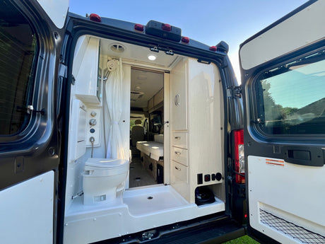 Rear view of open RV rental doors revealing a compact shower, toilet, and storage inside this modern camper van.