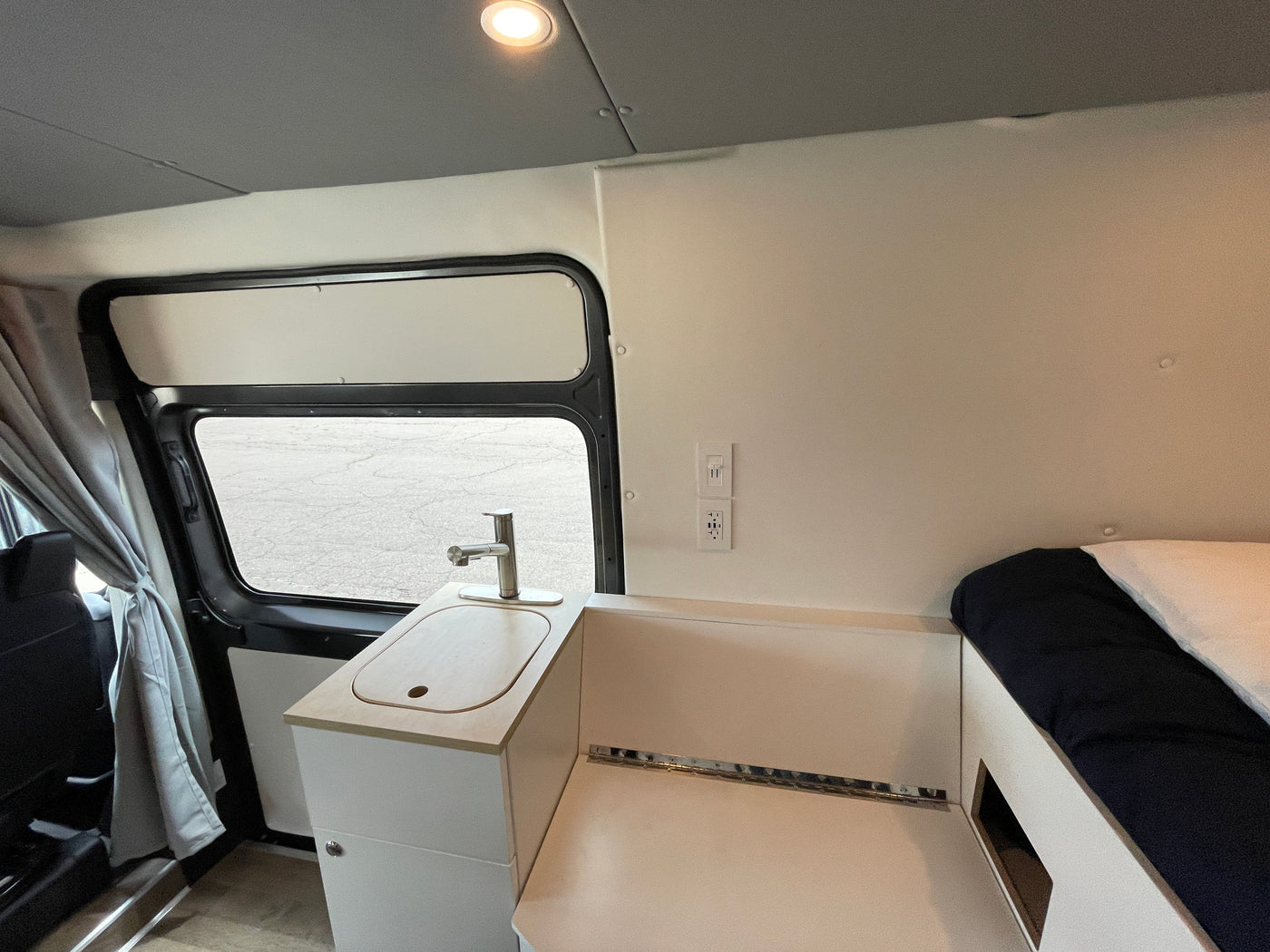 Interior of an RV rental featuring a compact kitchen with a sink, faucet, power outlets, and adjacent sleeping area. — photo 12