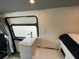 Interior of an RV rental featuring a compact kitchen with a sink, faucet, power outlets, and adjacent sleeping area.