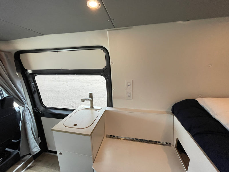 Interior of an RV rental featuring a compact kitchen with a sink, faucet, power outlets, and adjacent sleeping area. — photo 12