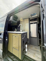 Modern rv rental interior: compact kitchen with sink, microwave, fridge, sleek controls, and wood-look flooring.
