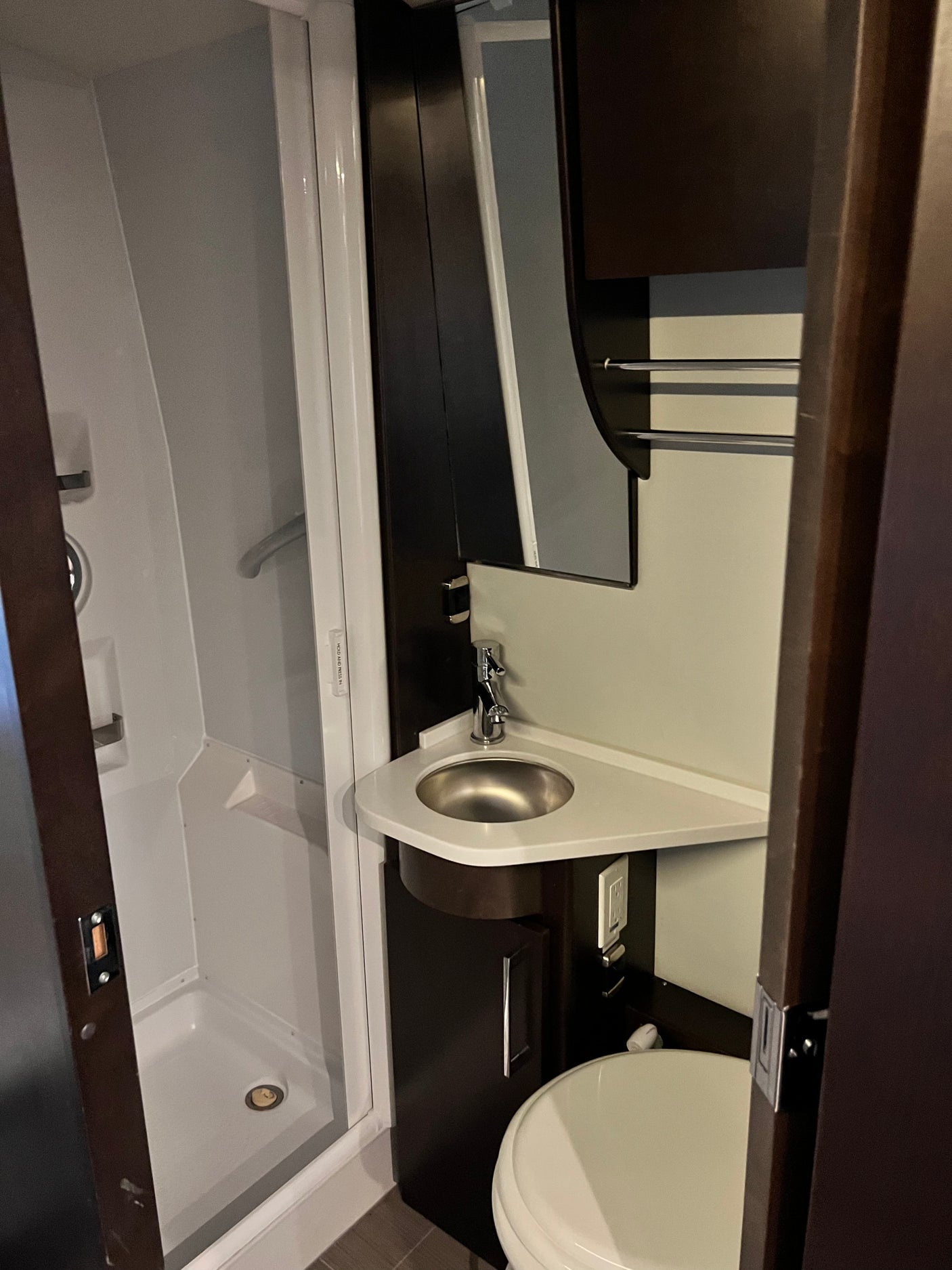 Efficient RV rental bathroom with shower, corner sink, toilet, and sleek dark cabinetry. Ideal for travel comfort.