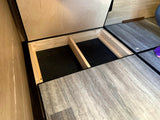RV rental: Open underfloor storage compartment with light wood framing and a dark, textured floor, useful for campervan gear.