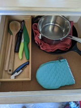 Organized RV rental kitchen drawer: wooden utensils, knives, peeler, corkscrew, pot, pan, & hot pad.