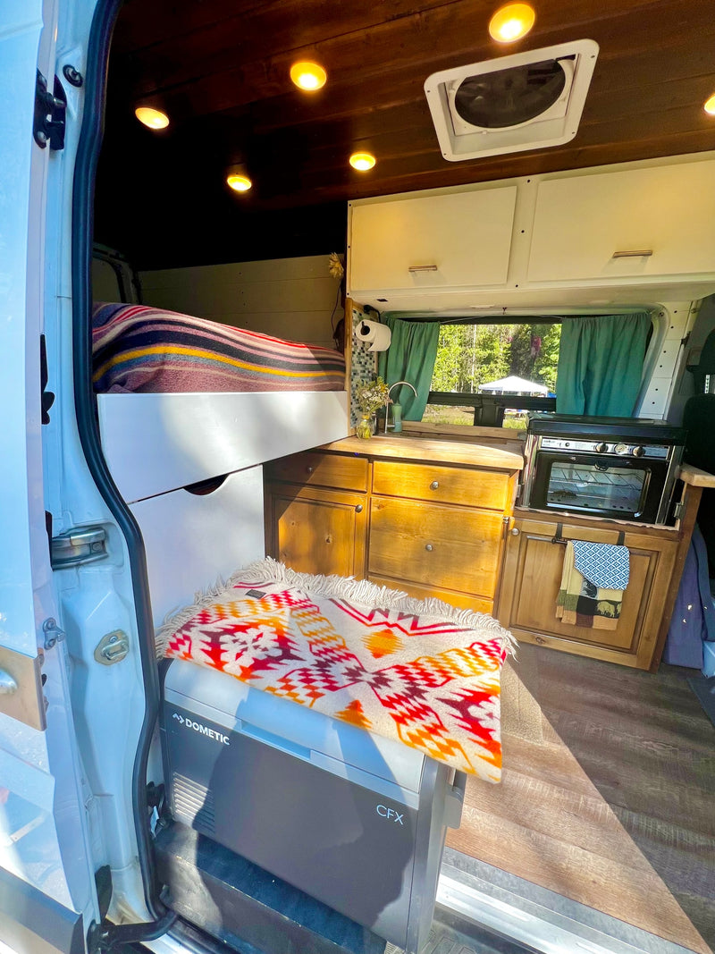 Cozy rv rental camper van interior. Features bed, kitchen, Dometic cooler & wooden accents. Ready for adventure! — photo 10