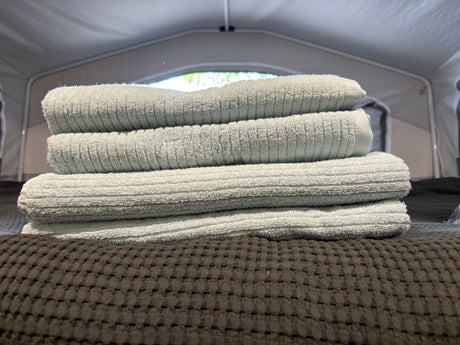Light blue towels stacked on a dark bed inside an RV rental, set for comfort on your journey.