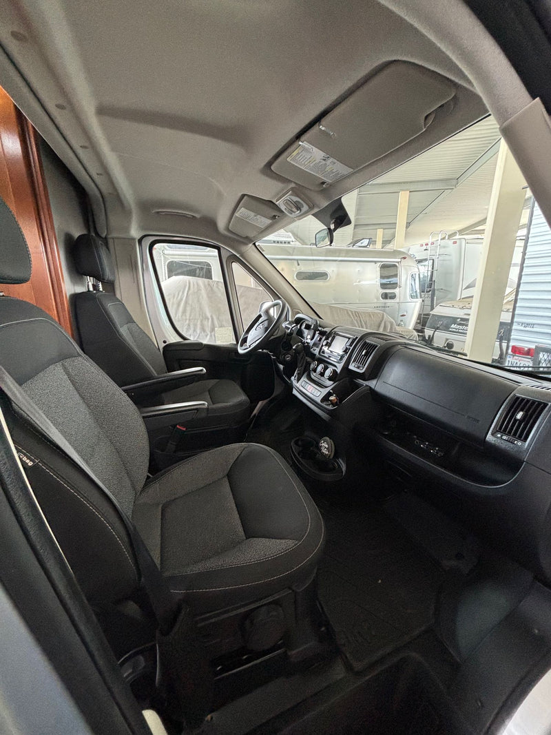  glowing campfire on sandy ground.|A light grey Pleasure-Way Lexor-TS RV with its side door open is parked at a sunny forest campsite. Great for an rv rental adventure!|RV rental front cabin view: driver's area — photo 3