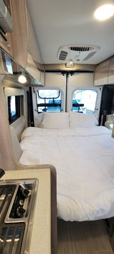 Cozy RV rental campervan interior features a comfy bed, windows, and a compact kitchen for your adventures.