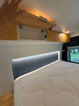 Cozy RV rental interior features overhead storage (one cabinet open), a quilted bed, and an illuminated headboard for comfort.