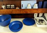 This RV rental kitchen setup features blue dishes, mugs, and a white basket of silverware, plus jars on the top shelf.