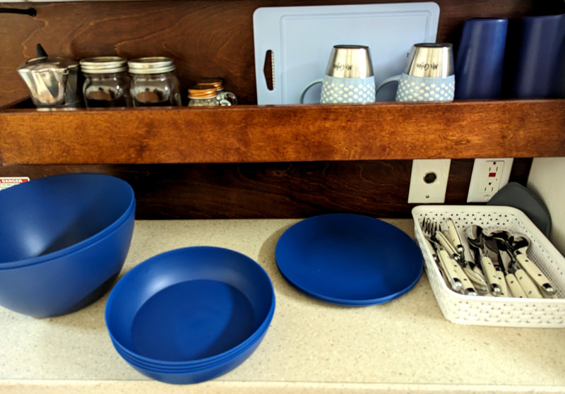 This RV rental kitchen setup features blue dishes, mugs, and a white basket of silverware, plus jars on the top shelf. — photo 6