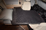 Cozy bed in an RV rental, featuring a grey pillow and patterned blanket extending towards the driver's seat and dashboard.