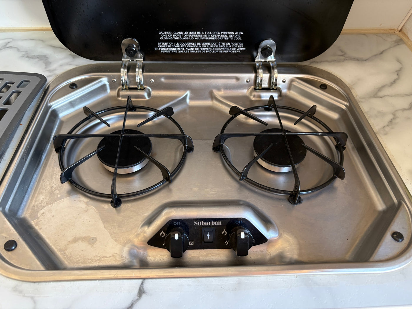 Suburban two-burner gas cooktop with open glass lid, control knobs, and igniter in an RV rental kitchen setup. — photo 4