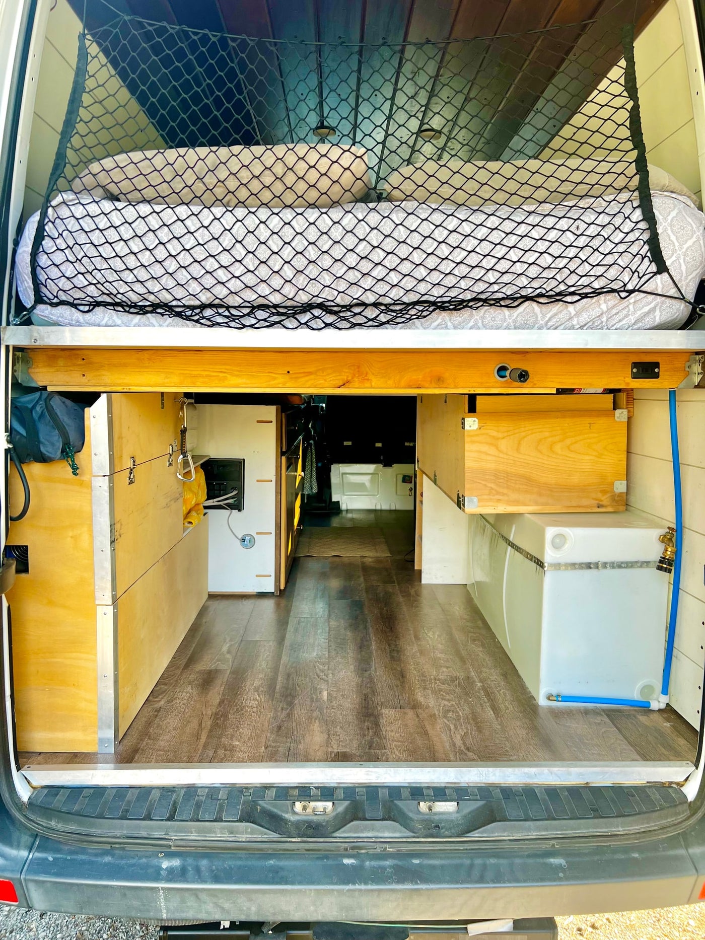 Camper van interior: Rear storage and bed platform of an RV rental, showing a water tank and custom cabinetry. — photo 15