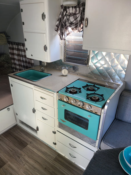 Explore this charming vintage RV rental interior with a vibrant teal kitchen, white cabinets, and wood-look flooring.