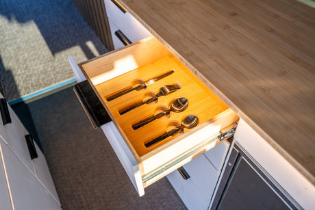 Thoughtful storage in an RV rental: An open drawer displays neatly arranged knives, forks, and spoons in a cutlery organizer.