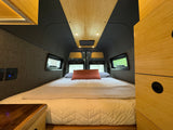 Relaxing RV rental interior showcasing a large bed, stylish wood ceiling & cabinetry, ambient lighting, and side windows.