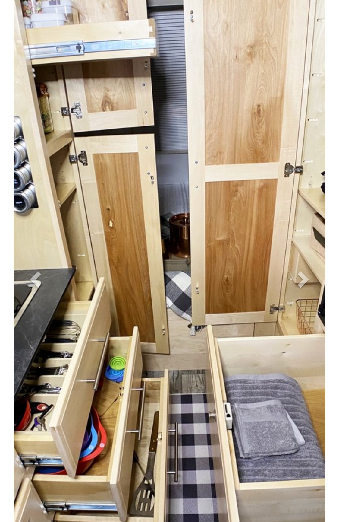 This RV rental interior features an organized kitchen with light wood cabinets, pull-out drawers displaying utensils & towels.