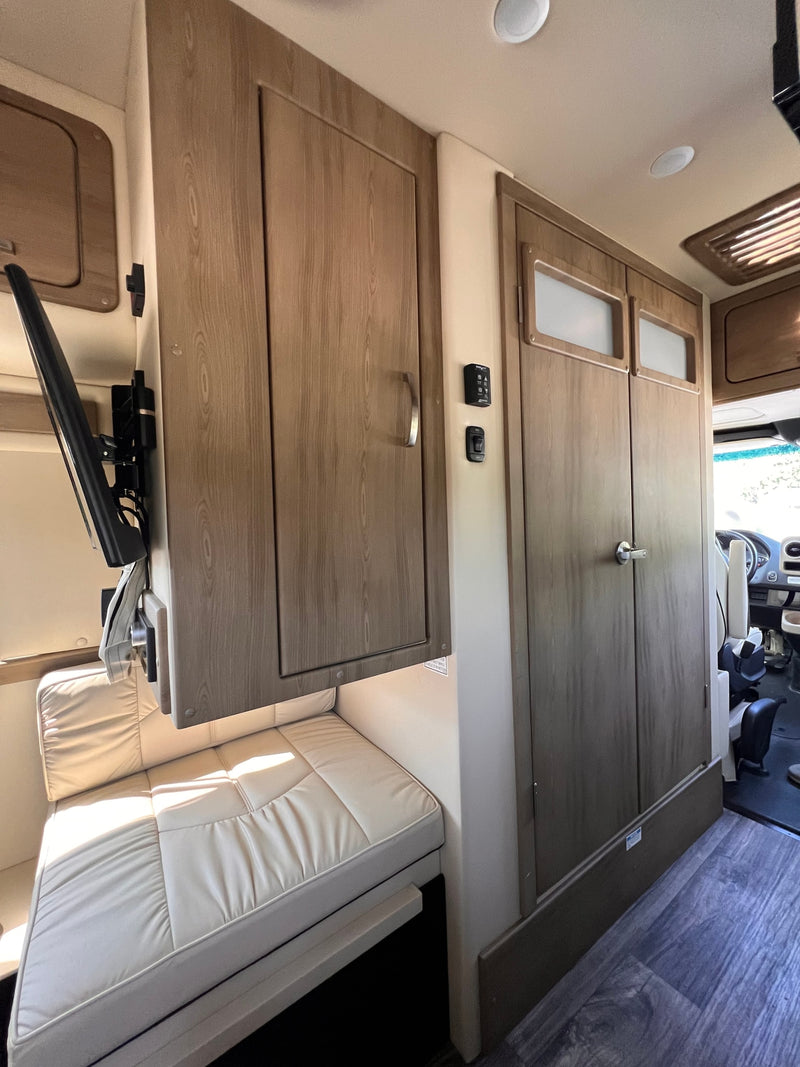 Cozy rv rental interior with light-colored seating, mounted TV, and wood-look cabinets, looking towards the cockpit. — photo 6