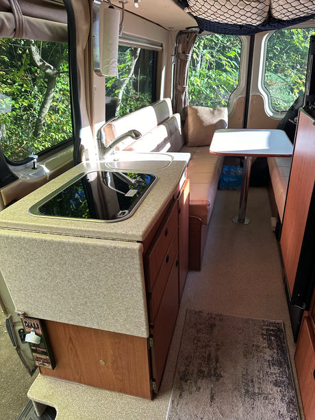 Explore this compact rv rental interior featuring a kitchenette, dining table, and cozy living space for travel.