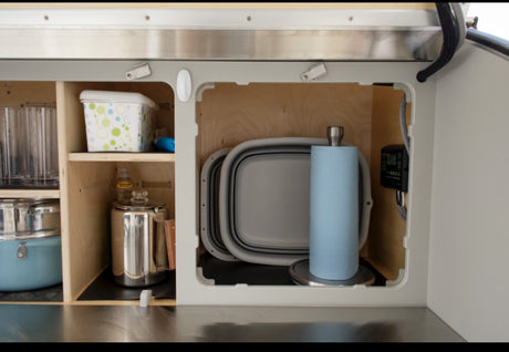 RV rental: Organized compact kitchen space with cookware, glasses, paper towels, & collapsible dishes.
